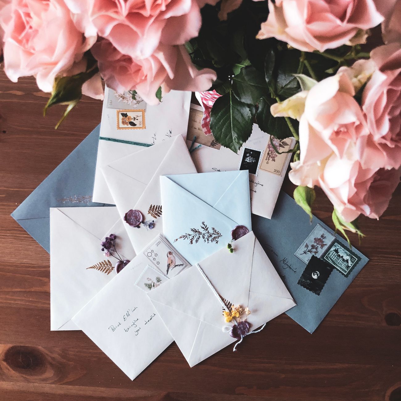 A stack of letters with sealing wax and flowers on a wooden desk.