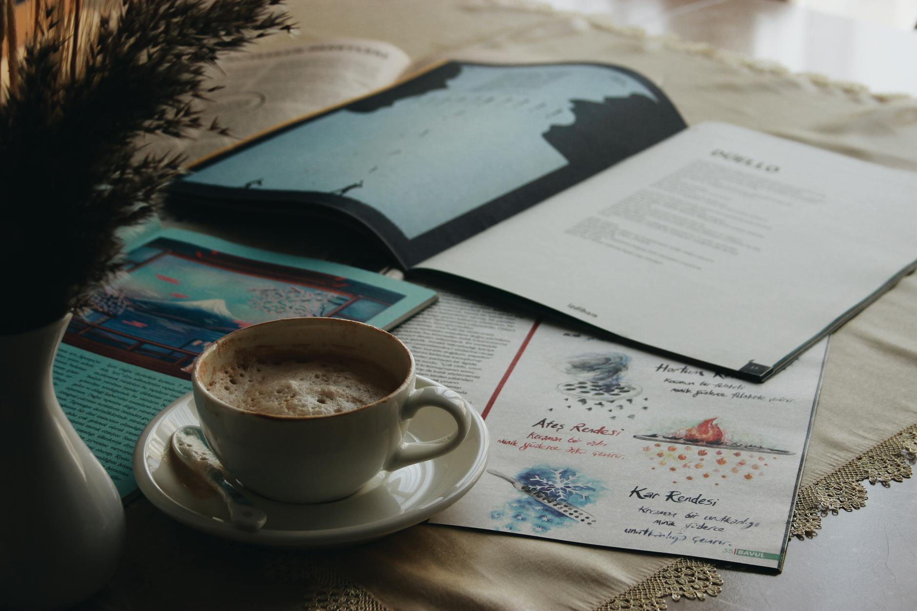 A warm cup of coffee near open magazines on a table.