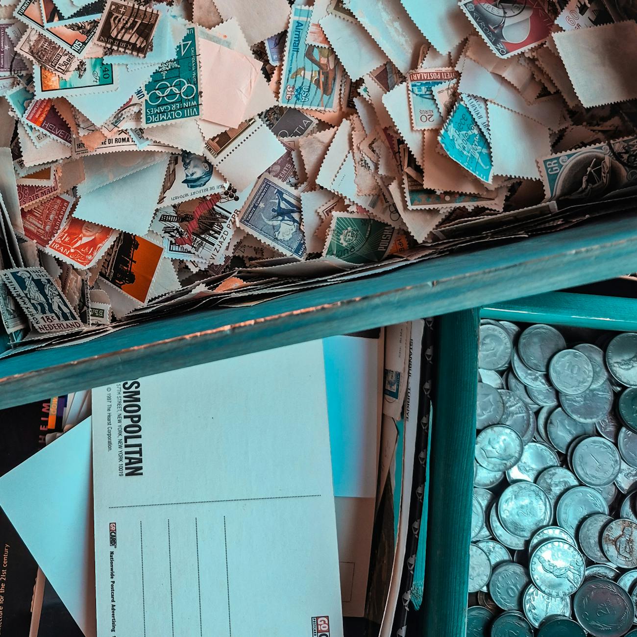 Vintage stamps, postcards, and coins in a collector's box.