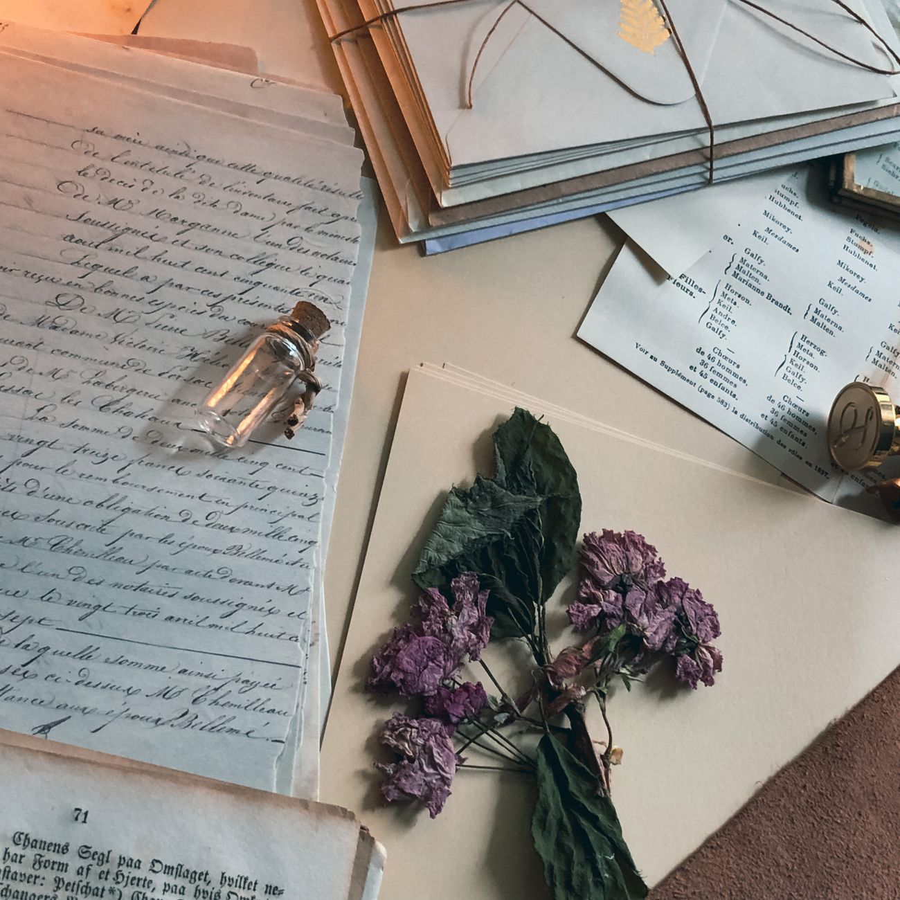 Vintage letters, dried flowers, and a small vial arranged on a desk.
