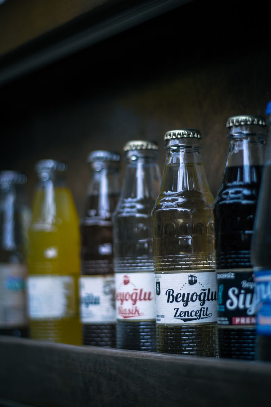 Beverage bottles with labels arranged on a wooden shelf.